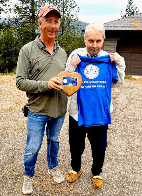 Jerome Wright and Todd Fahlstrom standing together with Jerome holding a new MAB tee-Shirt and Todd holding a heart shaped award to be given to Jerome.